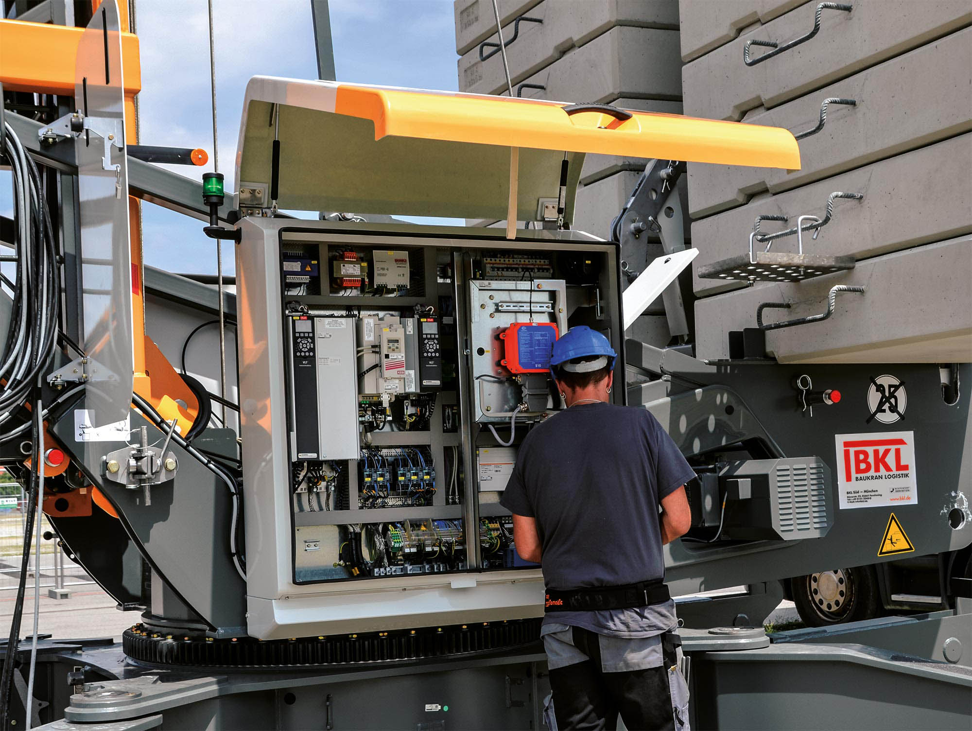 Techniker im blauen Schutzhelm überprüft die geöffnete Steuerung eines Krans mit BKL-Branding, was den professionellen Kranservice von BKL für Wartung, Reparatur und bei Notfall am Baukran bei Krananlagen zeigt.