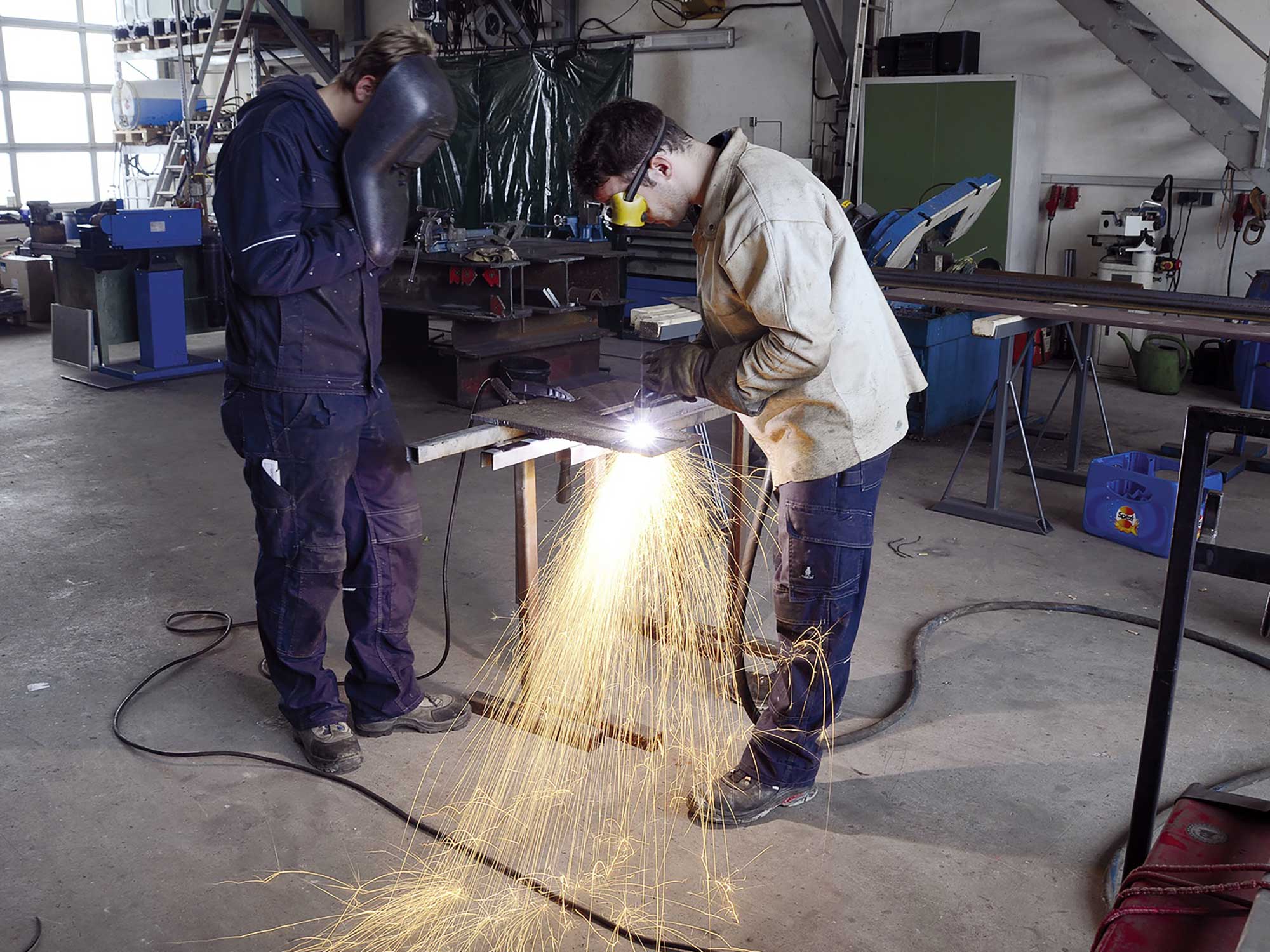 Auszubildende von BKL bearbeiten Metall in einer Werkstatt, mit Funkenflug bei der Ausbildung. Dieses Bild zeigt einen praktischen Ausbildungsplatz in der Baubranche und verdeutlicht den Karrierestart bei der Kranfirma BKL.