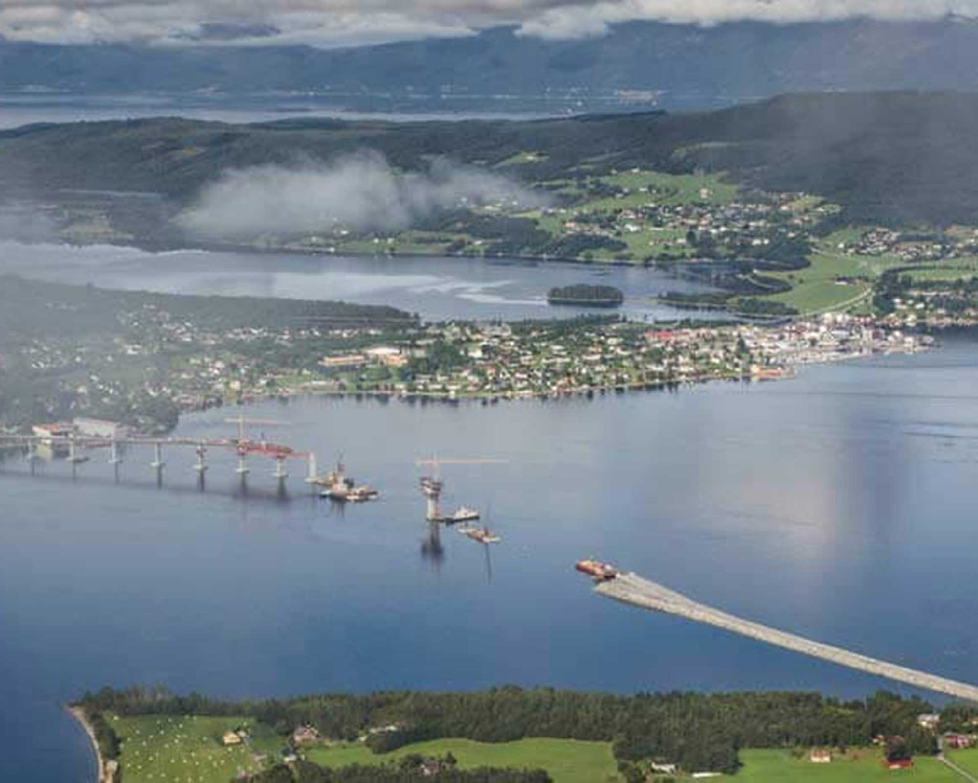 Bild von einer BKL Referenz am Tresfjord Norwegen: Luftaufnahme der über 1,2 Kilometer langen Brückenbaustelle über den Fjord. Ein BKL Mietkran ist für den Brückenbau und die Demontage im Einsatz.