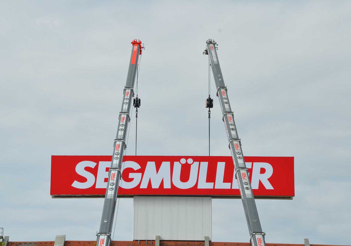 Zwei Liebherr Mobilkrane von BKL bei der Montage eines großen roten Segmüller Werbeschildes, professionelle Kranarbeiten für Industrie und Handel.