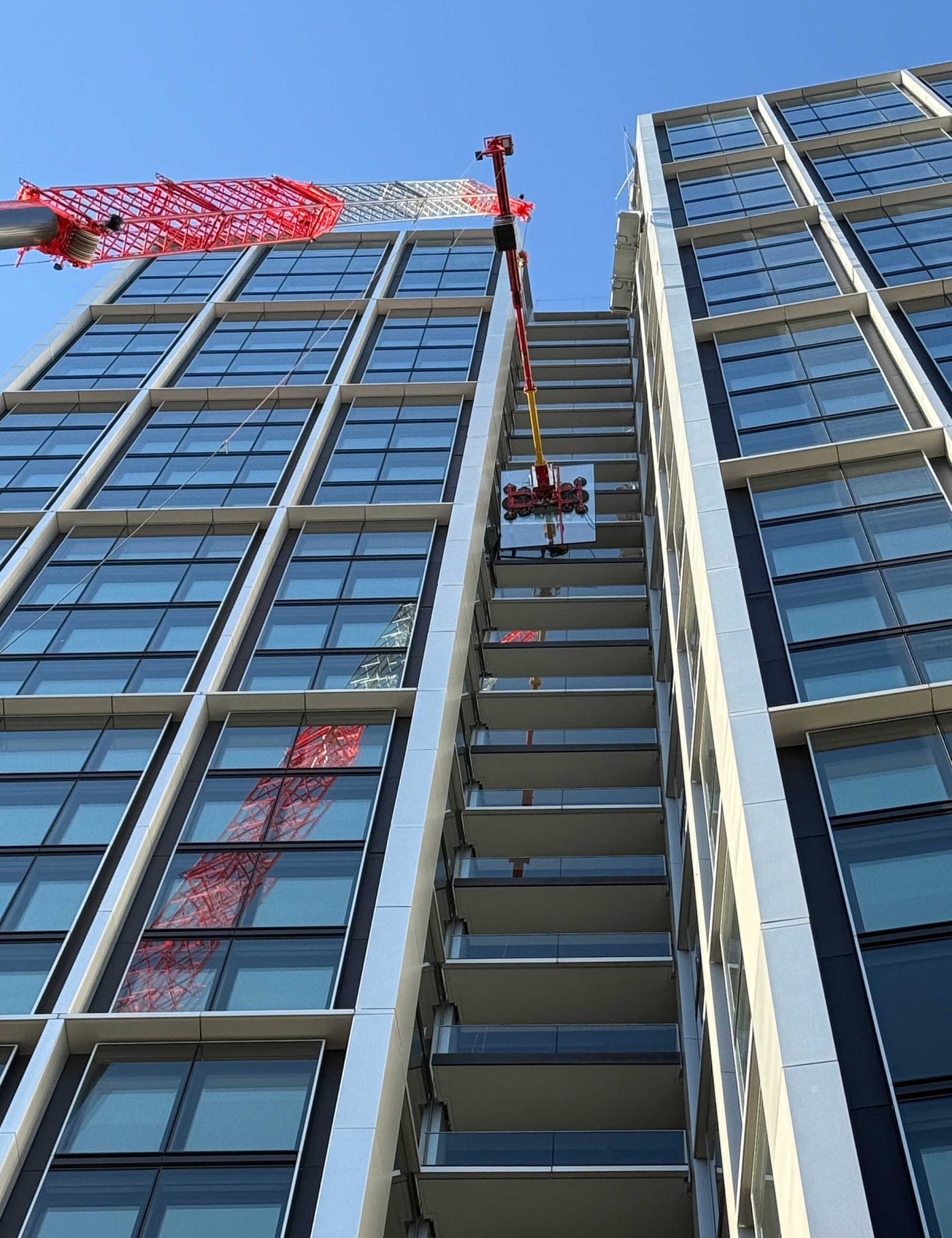 Zeigt eine Last, in diesem Fall eine Glasscheibe, die entlang der Glasfassade des Hochhauses Winx Tower in Frankfurt transportiert wird, demonstriert Kran-Einsatz in der Höhe mit BKL.
