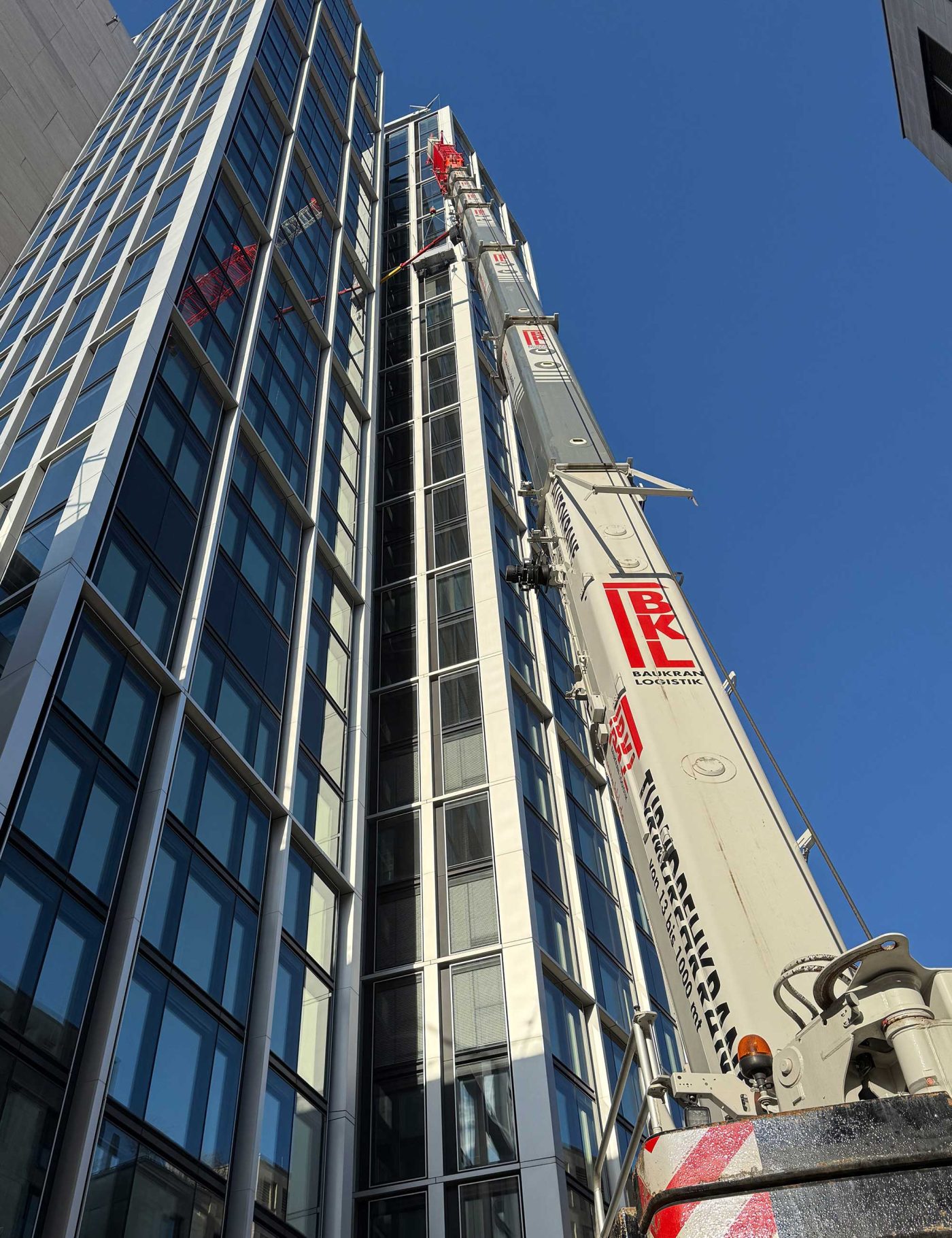 Ein Kran von BKL positioniert eine neue Glasscheibe an der Fassade des modernen WINX Towers in Frankfurt, veranschaulicht Glastausch und Hochhaus-Kranarbeiten.
