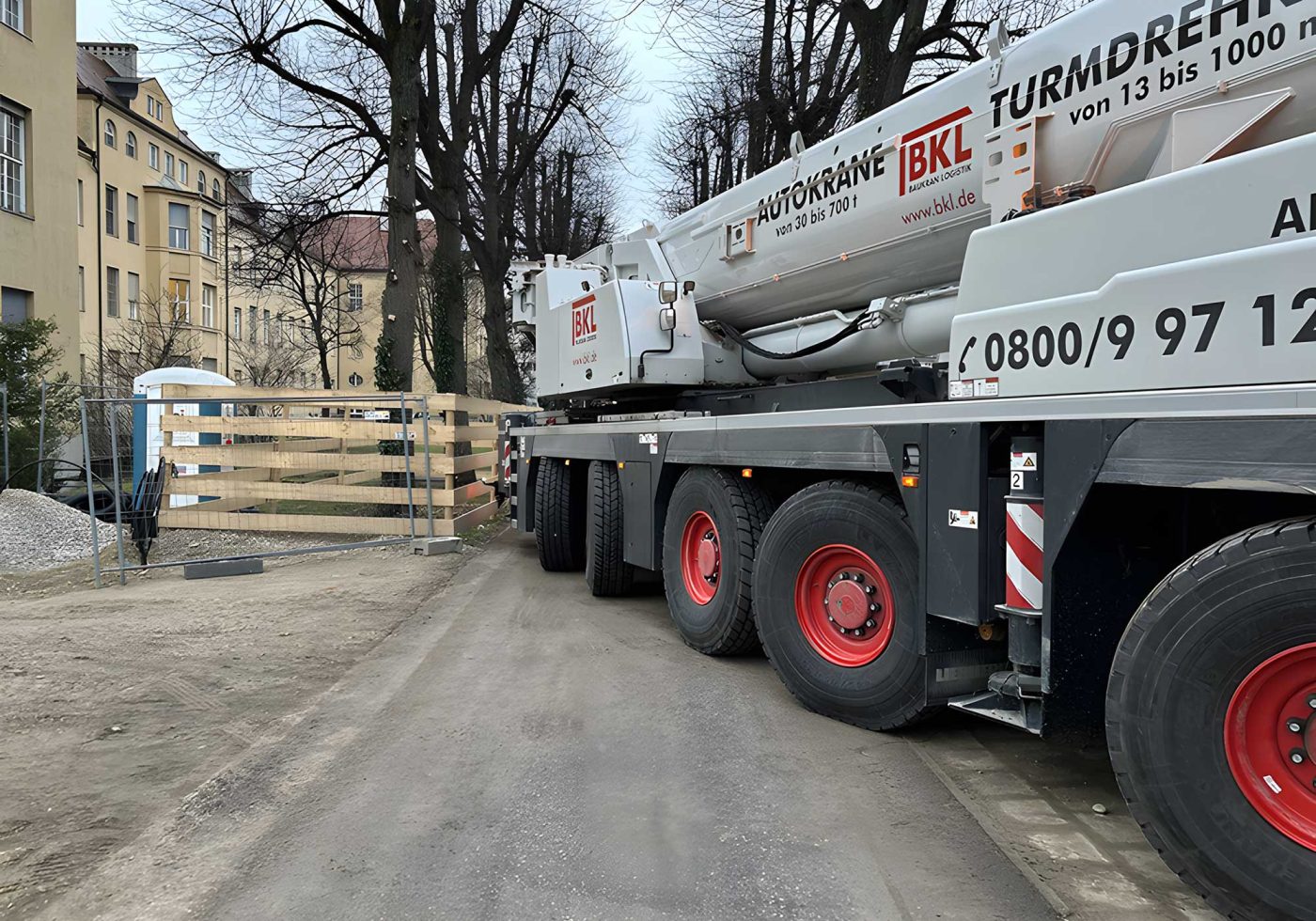 Großer BKL Autokran auf einer Baustellenzufahrt in städtischer Umgebung, bereit für Schwertransport oder Montagearbeiten.