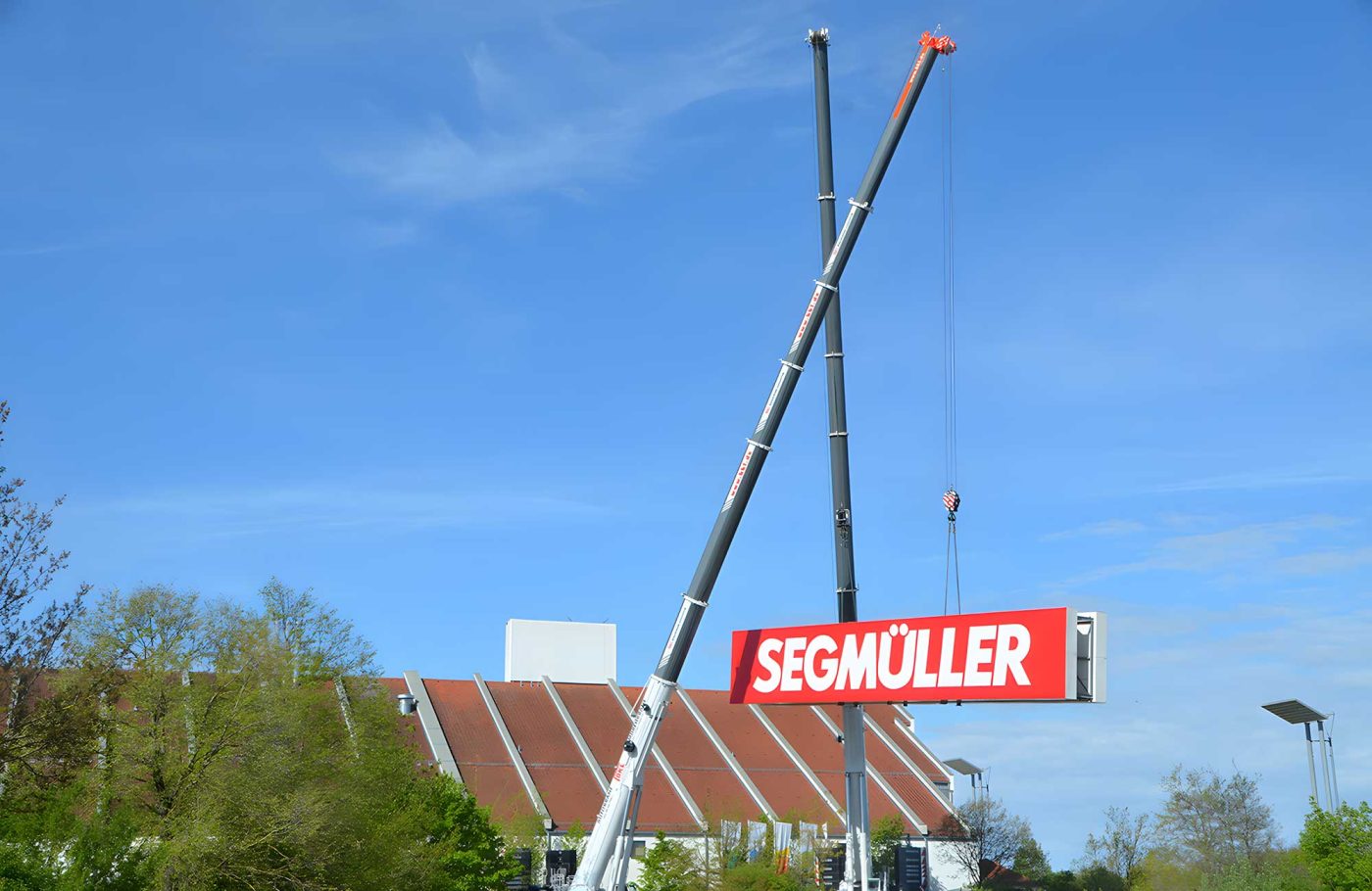 Zwei Mobilkrane von BKL montieren ein großes Segmüller Werbeschild, spezialisierte Hebearbeiten