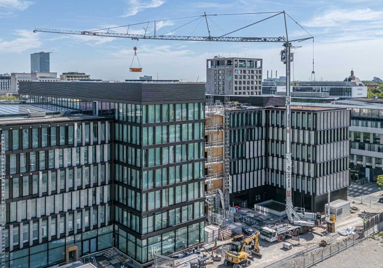 BKL Mobilkran auf einer Baustelle in der Stadt beim Heben einer Last zwischen modernen Bürogebäuden mit Glasfassaden
