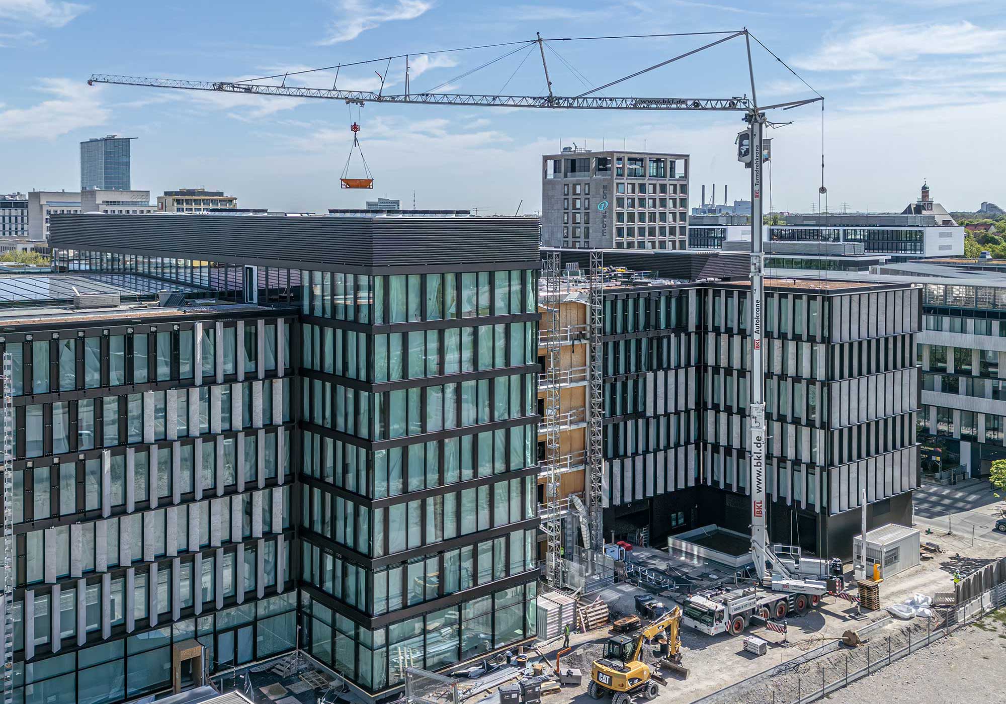 BKL Mobilkran auf einer Baustelle in der Stadt beim Heben einer Last zwischen modernen Bürogebäuden mit Glasfassaden