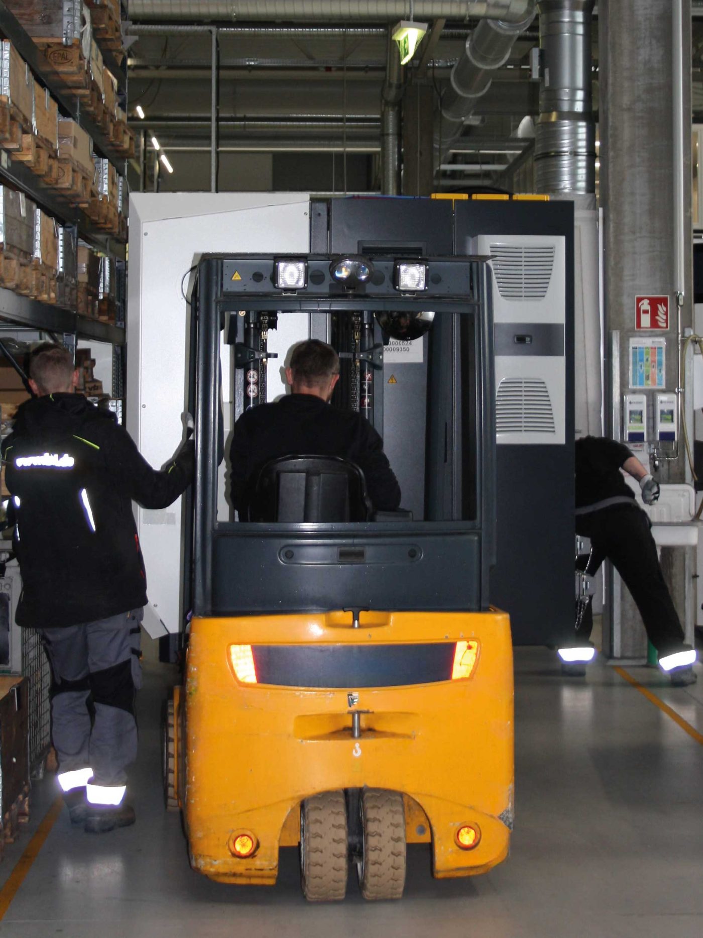 BKL-Mitarbeiter führen einen Maschinenumzug mit einem gelben Gabelstapler durch, um eine große Industriemaschine präzise für die Anlagenmontage zu positionieren.