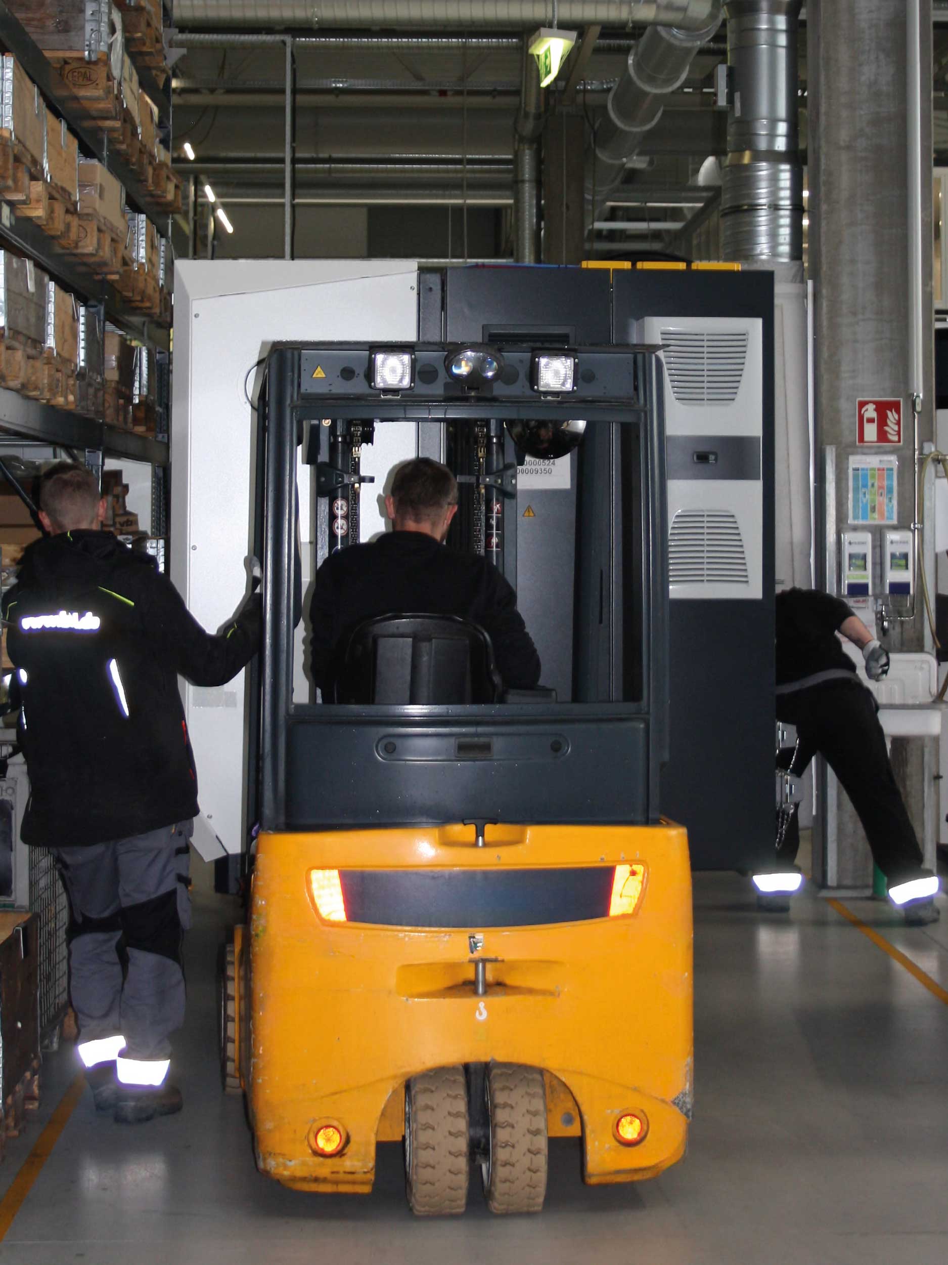 BKL-Mitarbeiter führen einen Maschinenumzug mit einem gelben Gabelstapler durch, um eine große Industriemaschine präzise für die Anlagenmontage zu positionieren.