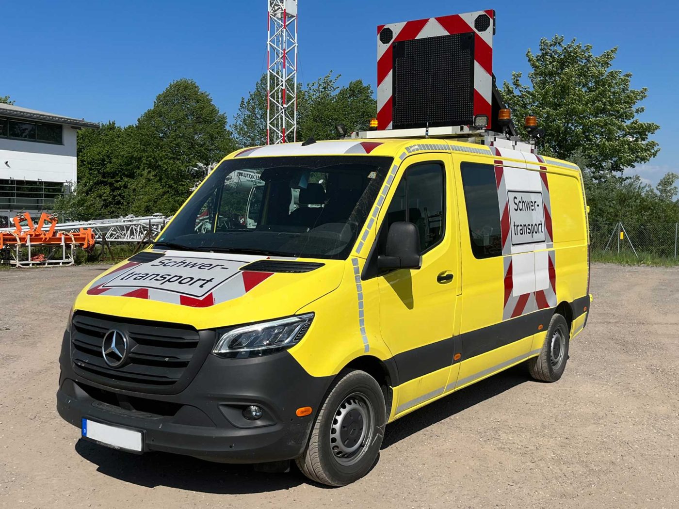 Gelber Mercedes-Benz Sprinter Begleitfahrzeug für Schwertransporte, ausgestattet mit rot-weißer Warnmarkierung, einem Dachdisplay und der Aufschrift "Schwertransport".