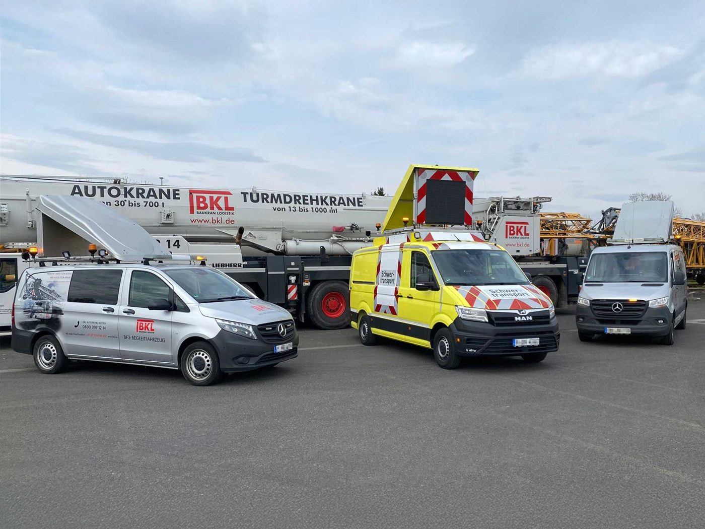 Drei BKL Begleitfahrzeuge, darunter ein gelber Van und ein silbernes Begleitfahrzeug, stehen vor einem Großraumtransport mit Kranteilen. Das Bild veranschaulicht BKLs umfassende Logistik für Krantransporte und professionelle Transportbegleitung.