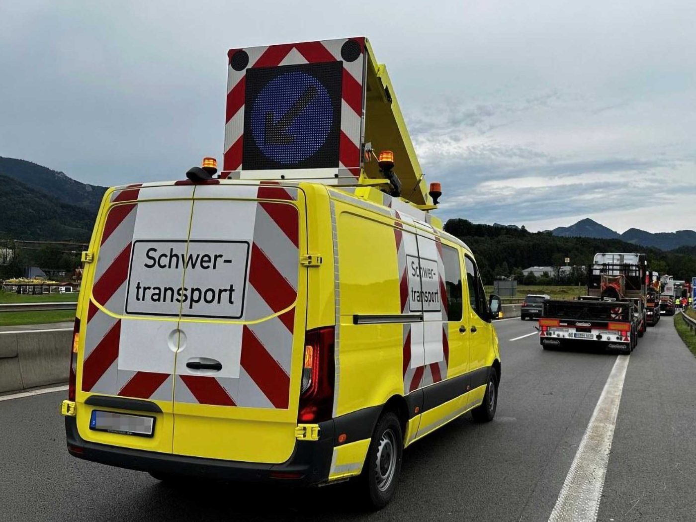 Gelber Begleitwagen mit 'Schwer-transport' Beschriftung und digitaler Warnanzeige sichert einen Schwertransport auf der Autobahn ab. Das Fahrzeug steht für die professionelle Transportbegleitung von BKL bei Großraum- und Spezialtransporten.
