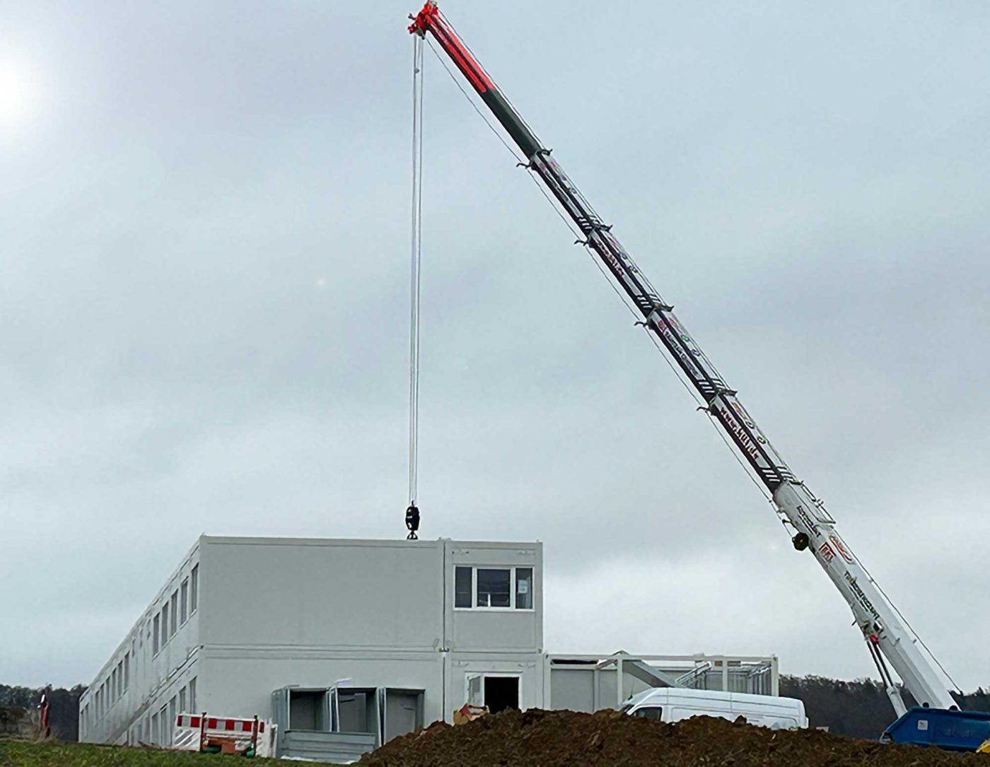 Ein Autokran montiert ein Raummodul für eine BKL Containeranlage im Modulbauweise, mit weiteren Containern im Hintergrund auf der Baustelle.