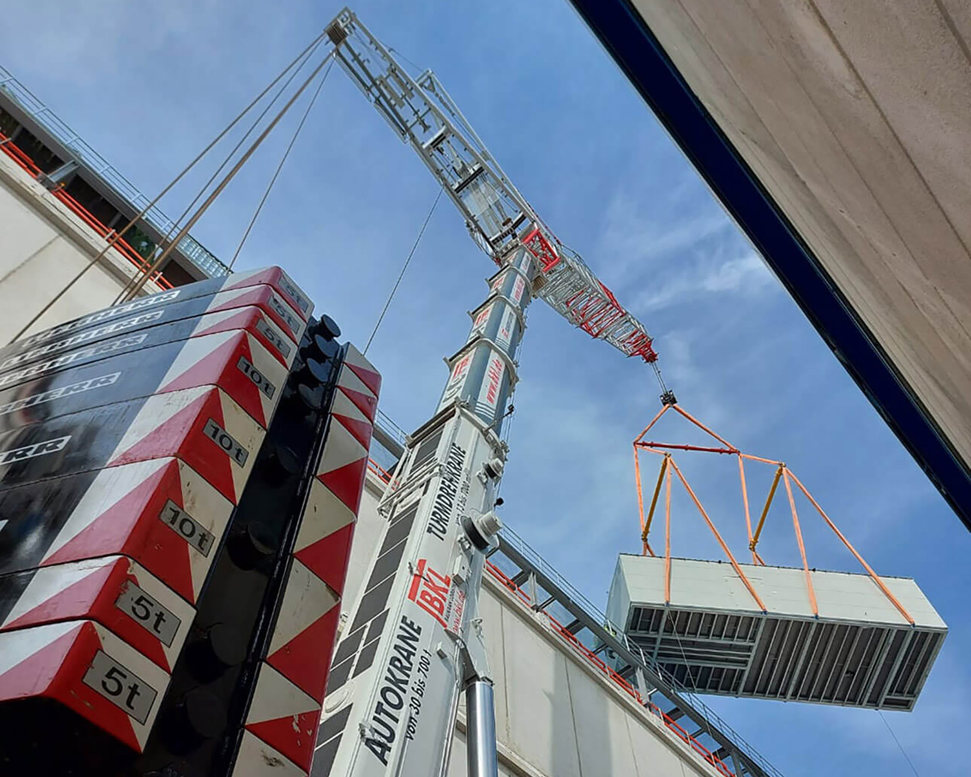 A mobile crane LTM 1450 with luffing jib and spreader beam from BKL Baukran Logistik lifts a heavy load between 2 houses.