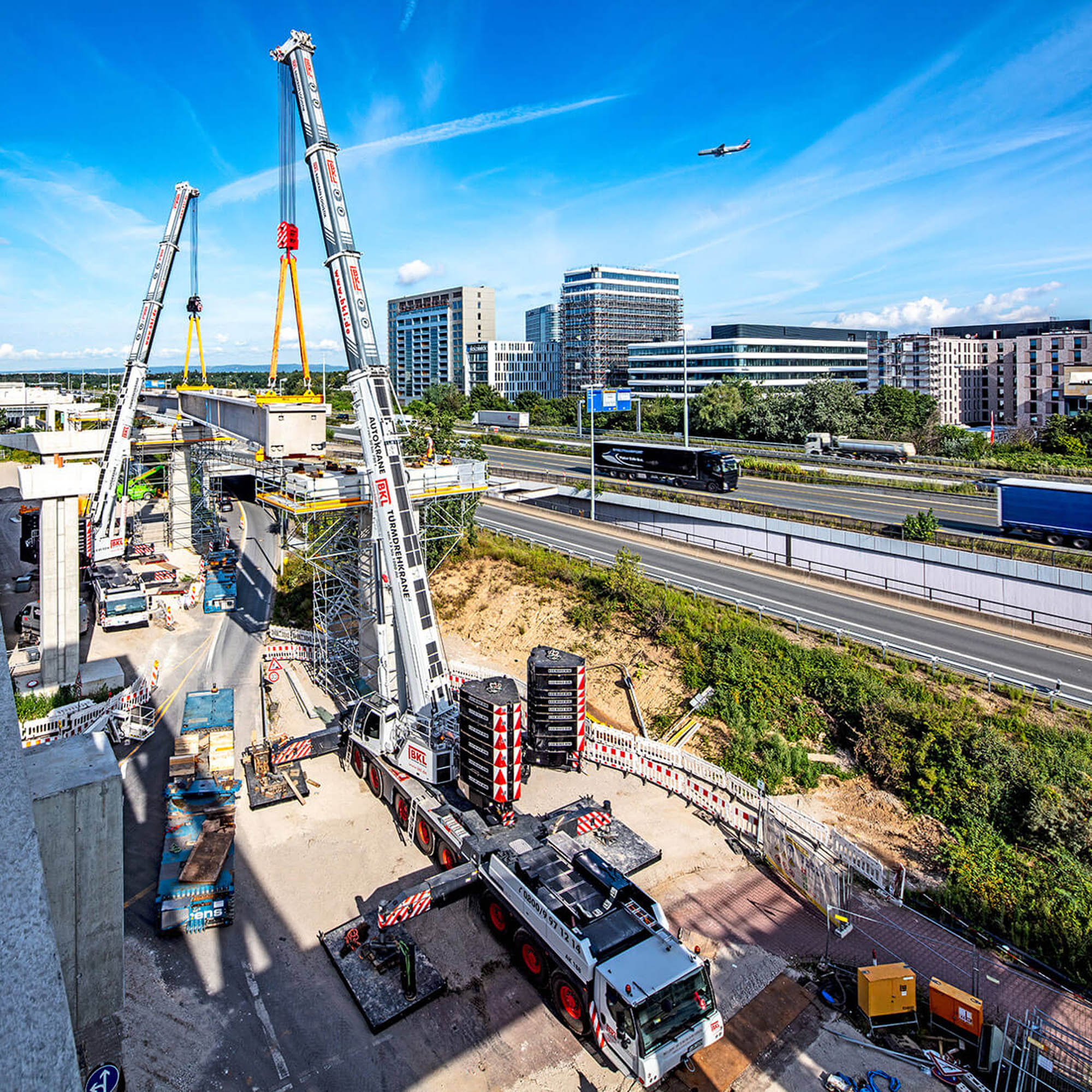 BKL mobile crane assembling a turret crane at a construction site under a blue sky