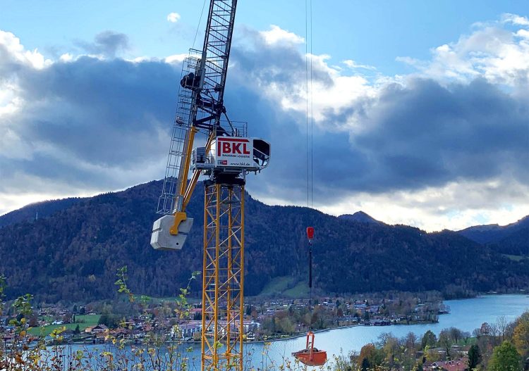 Wippkran in Hanglage vor einem See bei Hebearbeiten an einem Neubau