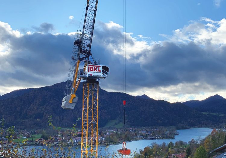 Wippkran in Hanglage vor einem See bei Hebearbeiten an einem Neubau