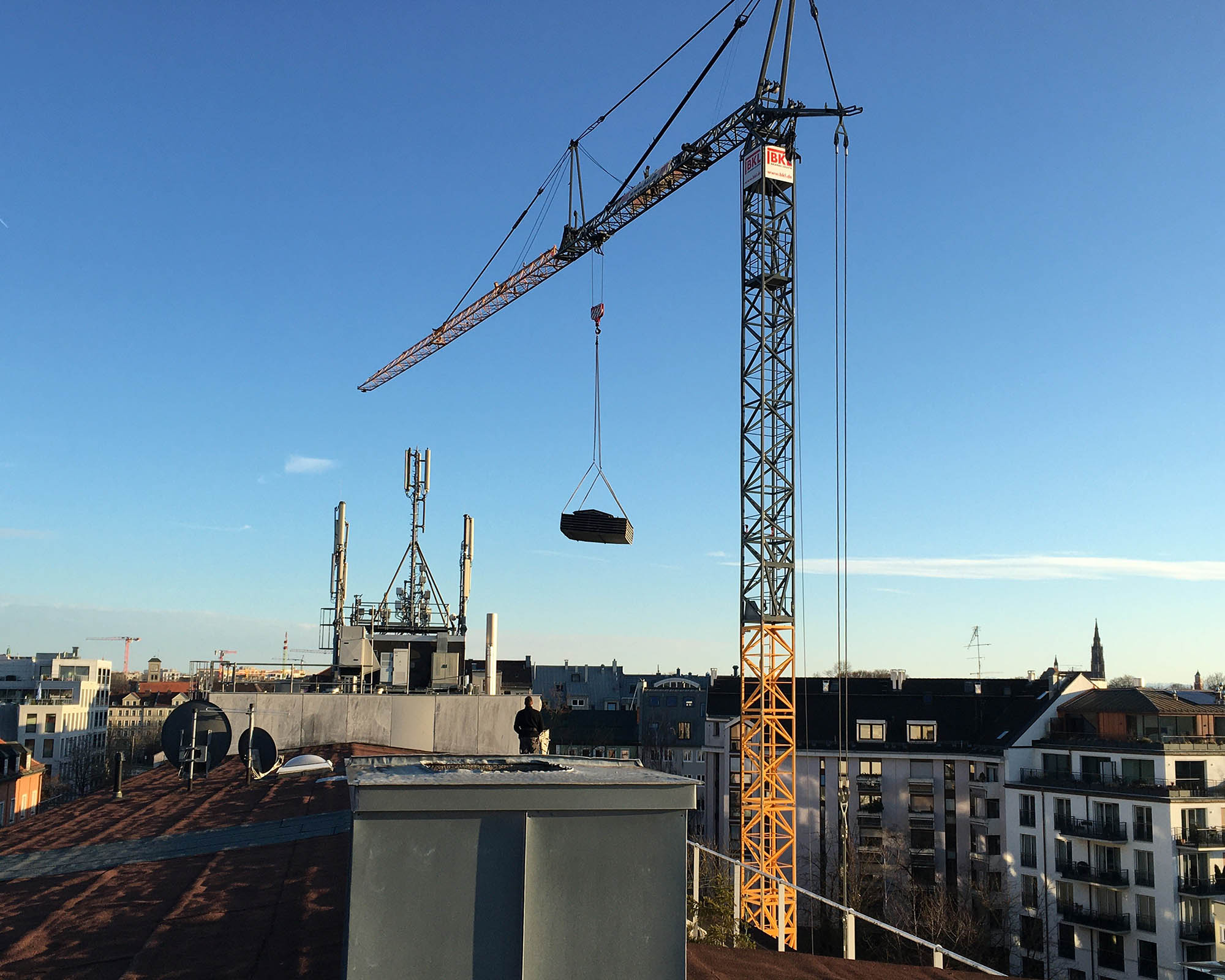 BKL bottom-slewing crane during lifting operations over the roofs of a city construction site under a blue sky