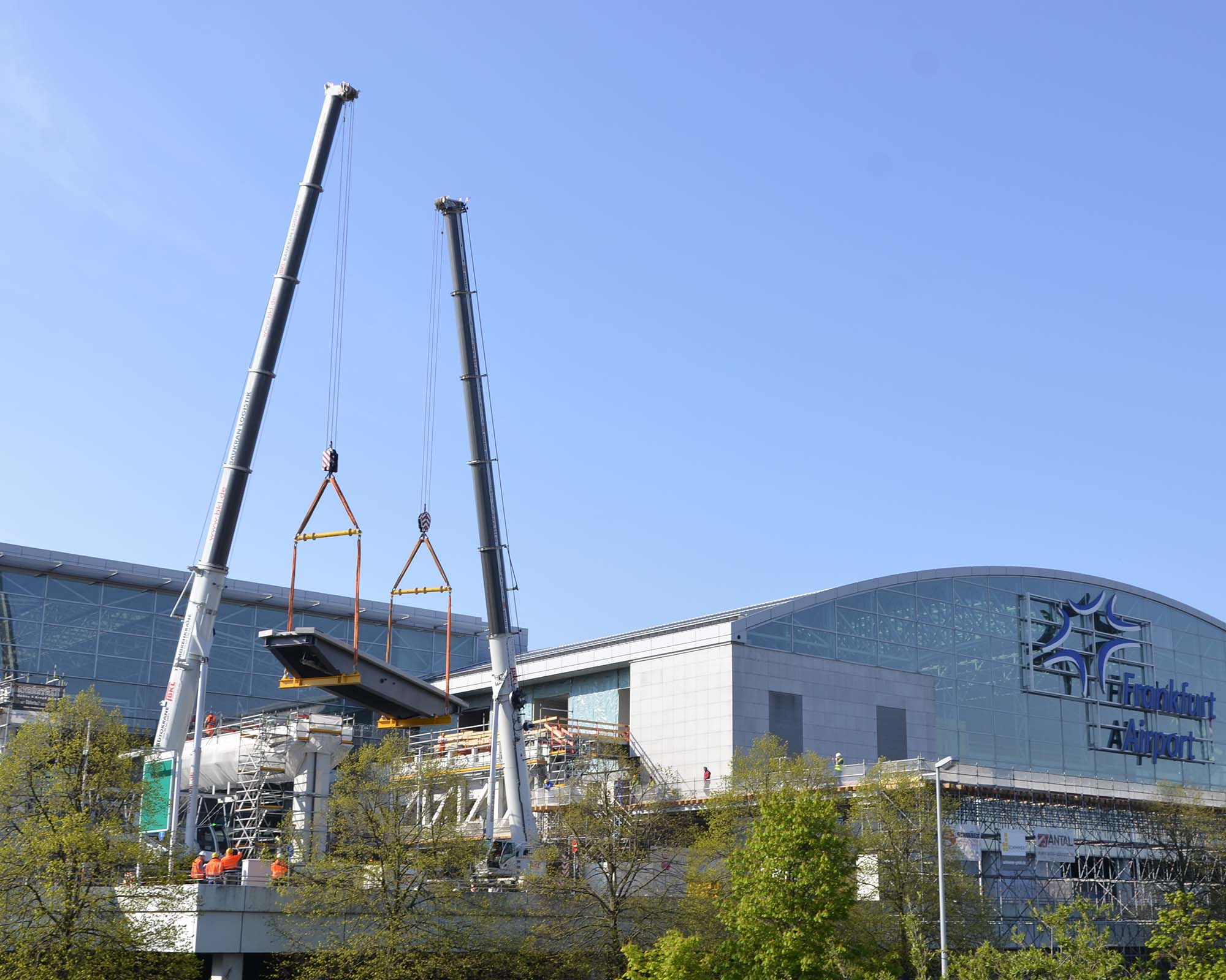 Die Autokrane LTM 1300-6.2 und GMK5250XL-1 aus dem BKL Mietpark heben im Tandemhub einen Stahlträger vor dem Gebäude des Frankfurt Airport
