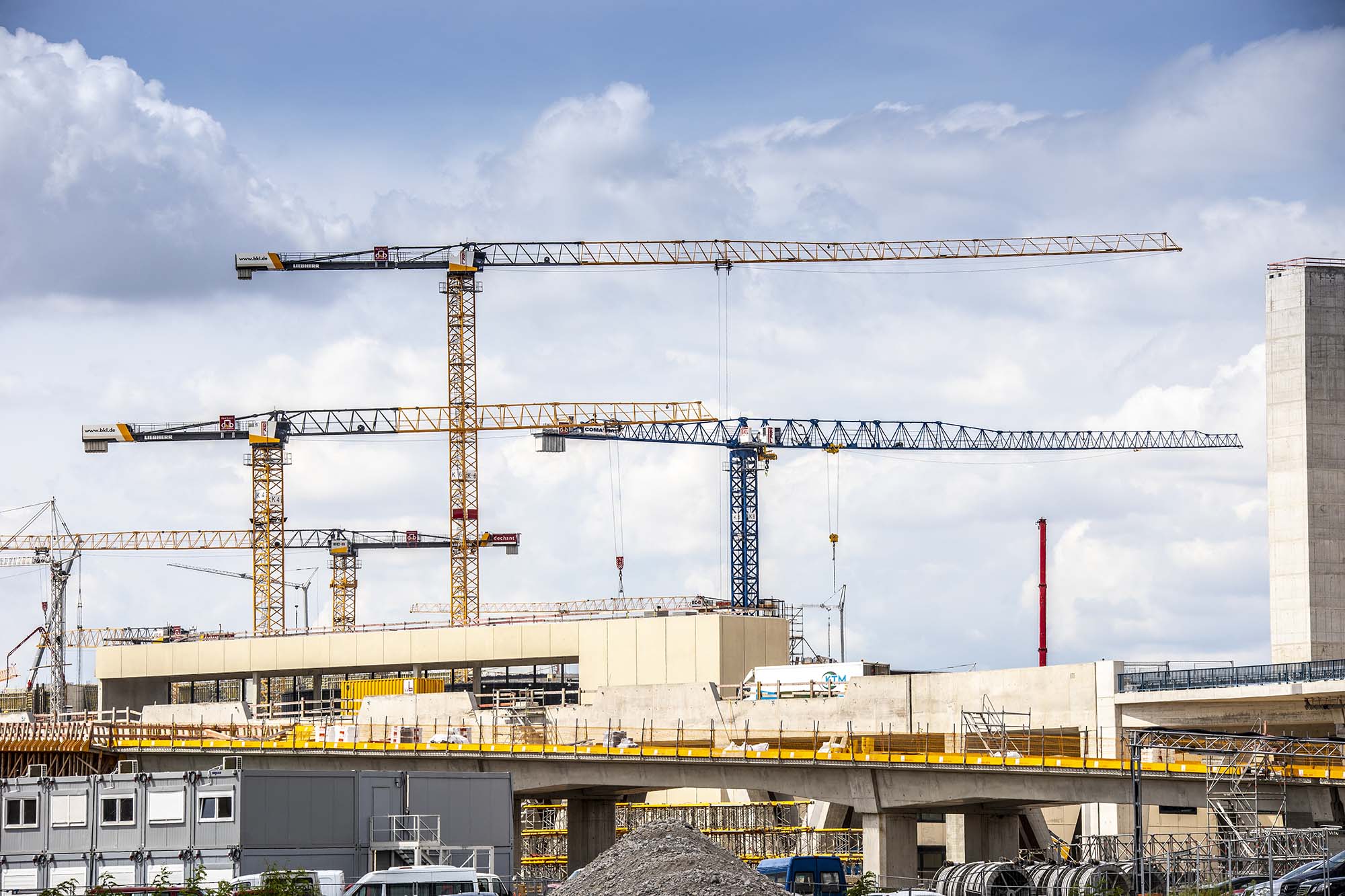 Several BKL construction cranes, including yellow Liebherr cranes, on a large construction site with shell buildings and construction containers, illustrating the construction progress and the comprehensive services of BKL crane rental and logistics.