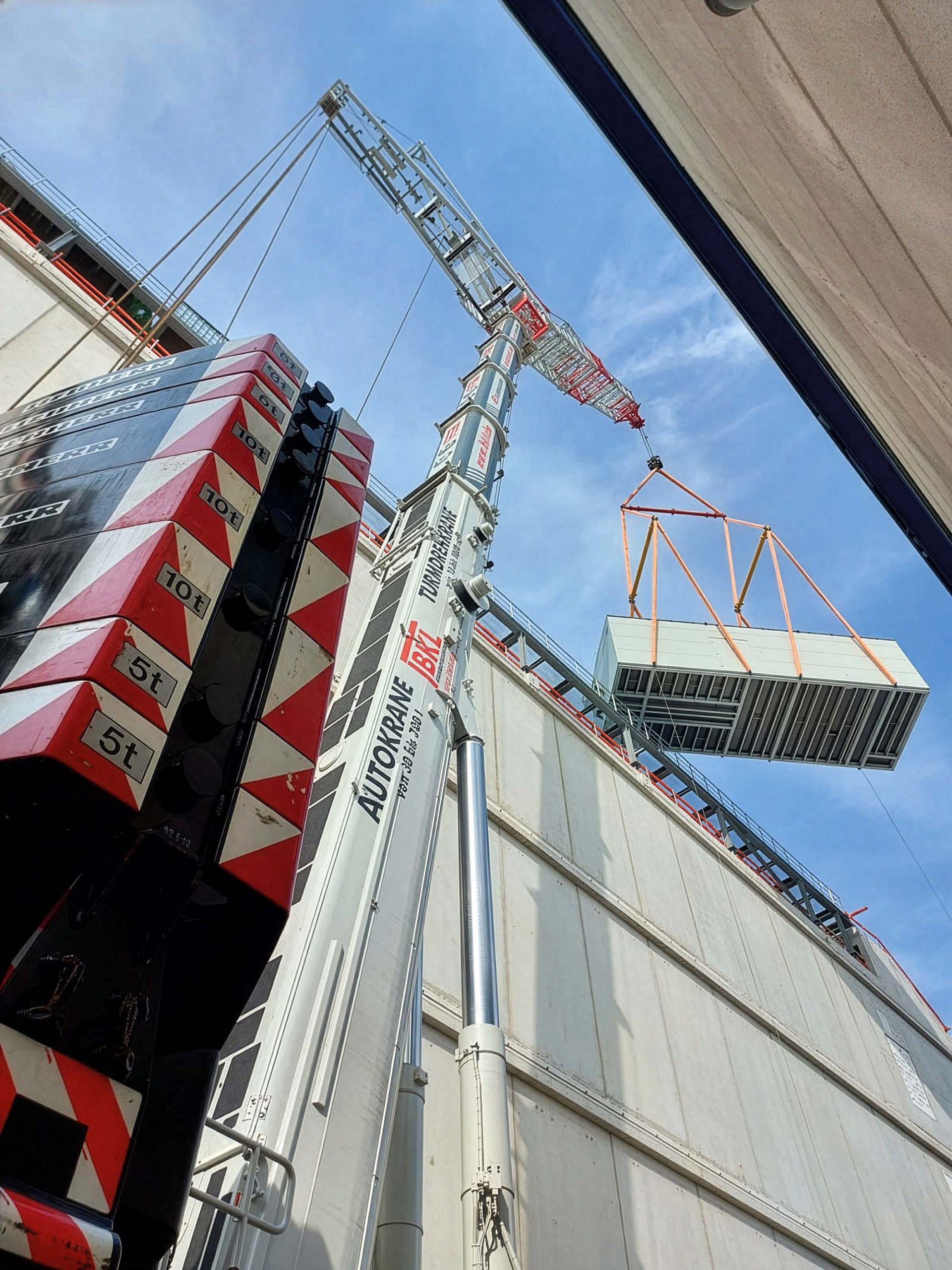 A mobile crane LTM 1450 with luffing jib and spreader beam from BKL Baukran Logistik lifts a heavy load between 2 houses.